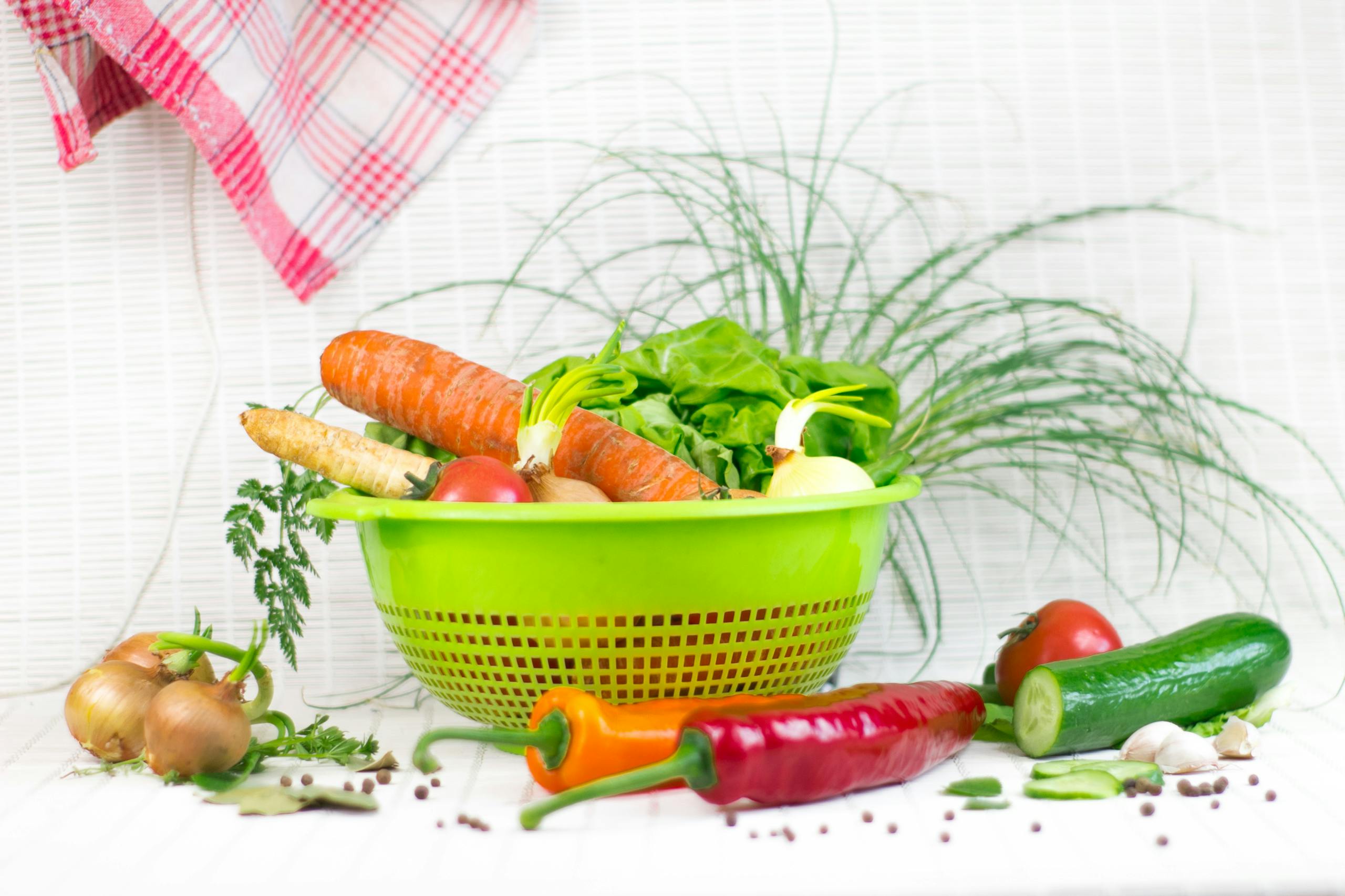 A vibrant assortment of fresh, organic vegetables in a green colander, ideal for healthy cooking and salads.