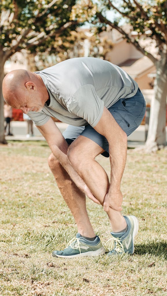 Man holding his injured ankle outdoors in a park, highlighting running-related pain or sport injury.