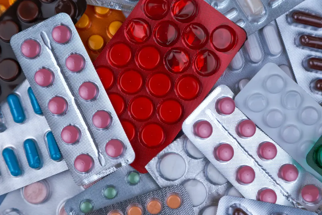 Assortierte Blisterpackungen mit verschiedenen Pillen und Kapseln in unterschiedlichen Formen, Größen und Farben, die verstreut angeordnet sind.