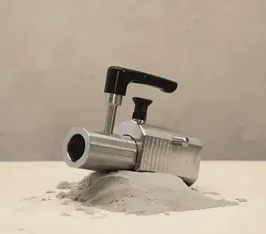 Ein Metallwerkzeug, das einer Kartuschenpistole ähnelt, steht auf einem Haufen grauen Pulvers vor einem schlichten beigen Hintergrund.